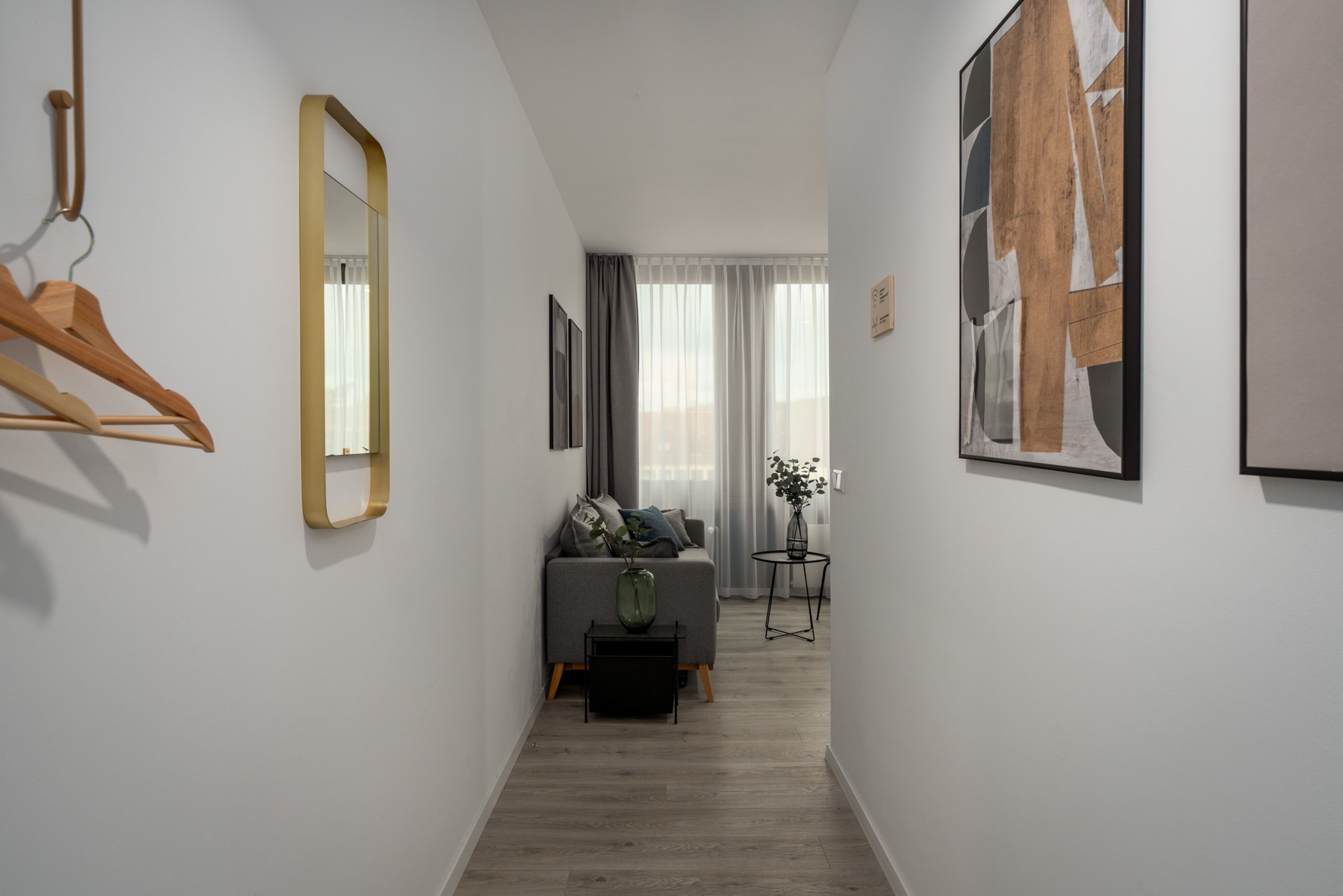 Ein schmaler Flur mit einer Couch, einem kleinen Tisch mit einer Vase und einem Spiegel an der Wand.