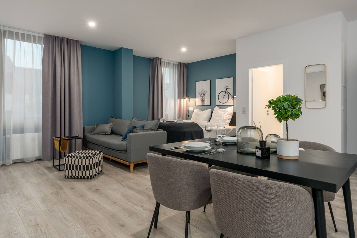 Een moderne woonkamer met een grijze bank, een eettafel met stoelen en een potplant.