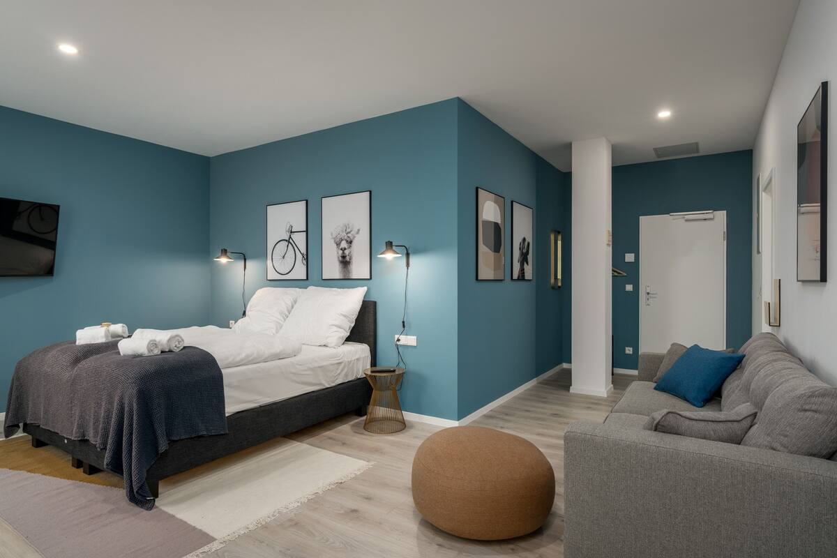 Een moderne slaapkamer met een bed, nachtkastjes, een bank en een rond poef.