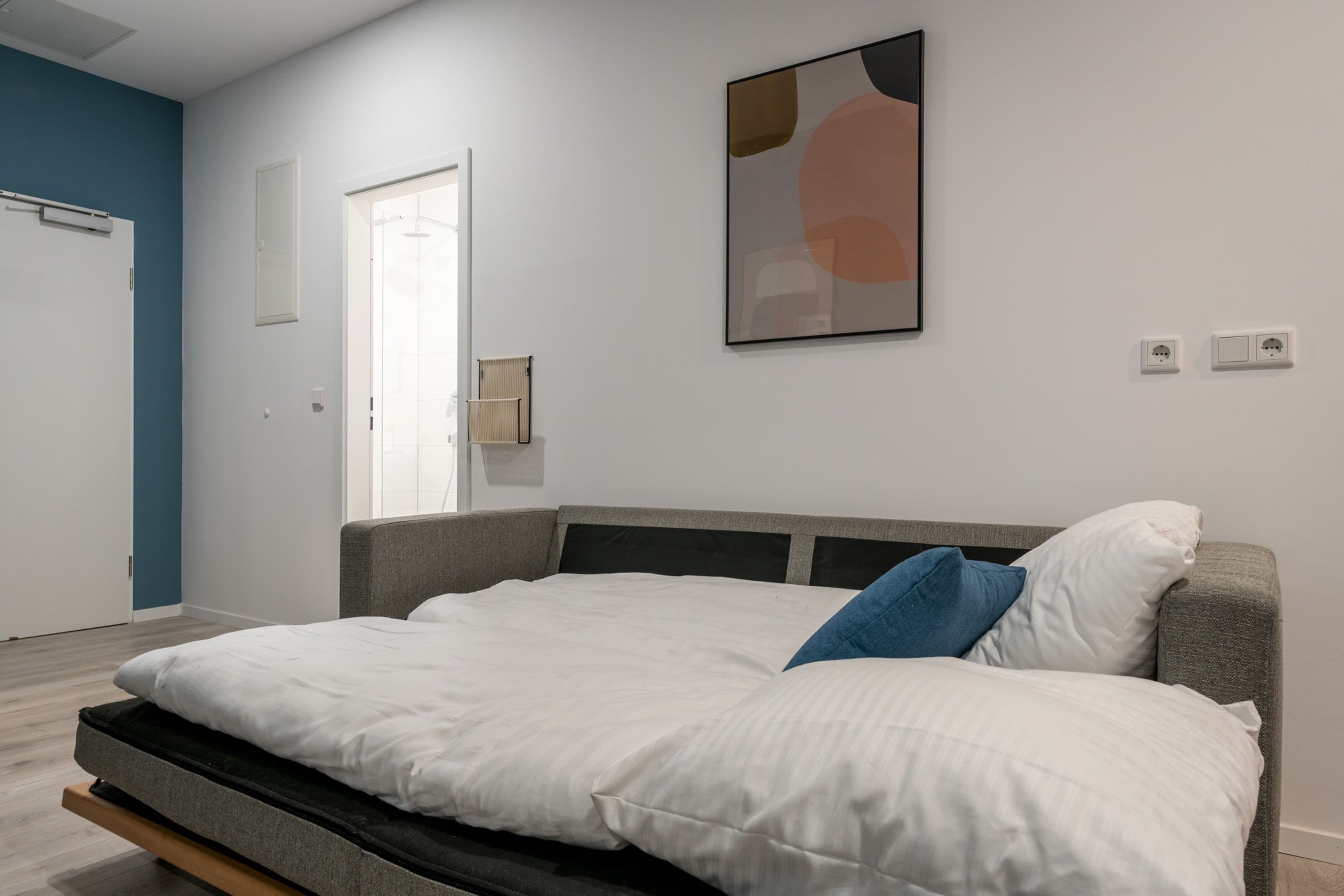 A modern bedroom with a bed, a door, and a wall-mounted light fixture.