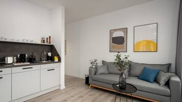 A modern living room with a grey sofa, a coffee table, and a kitchen area with white cabinets and a grey countertop.