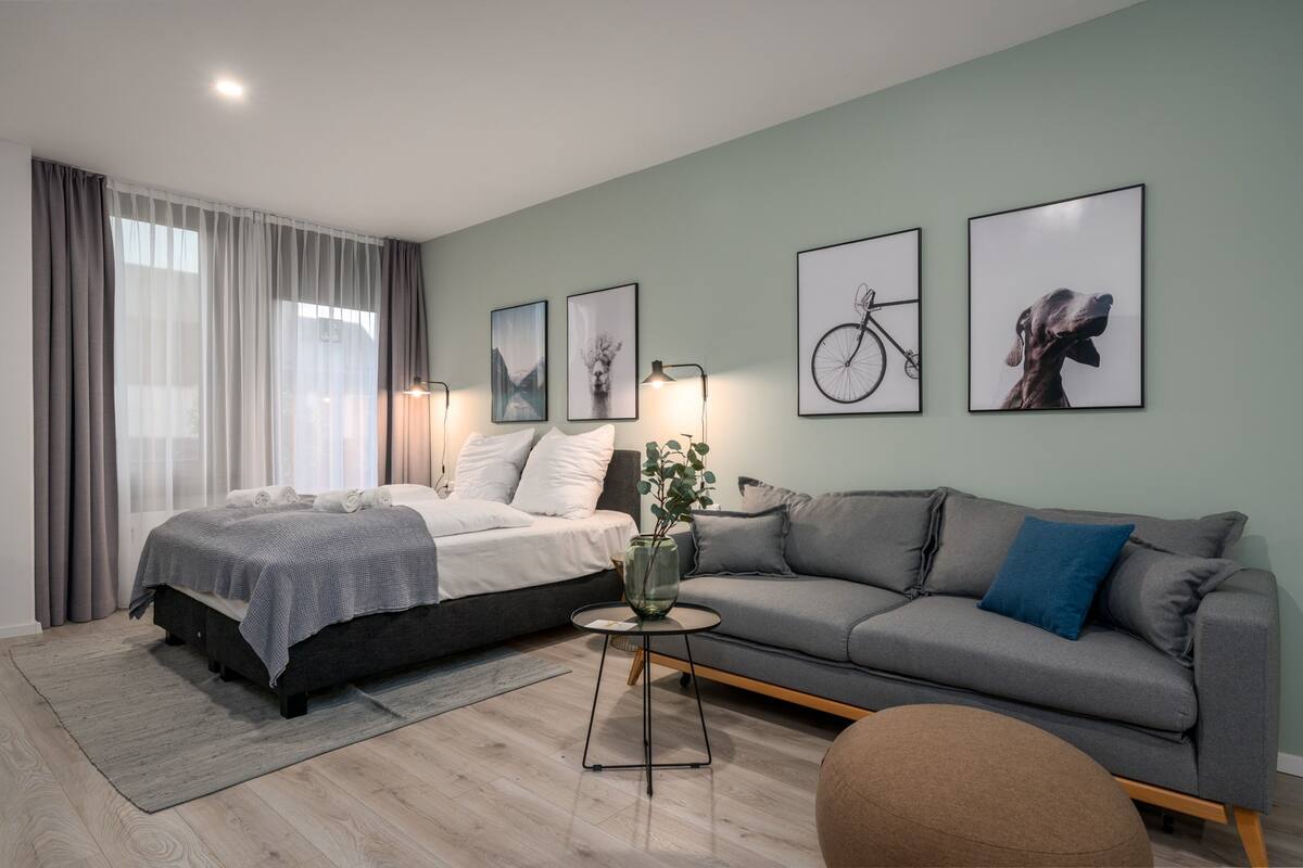 Een moderne slaapkamer met een bed, een grijze bank en een klein tafeltje met een vaas.