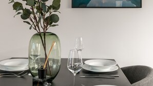 A dining table set with plates, cutlery, and a vase with green foliage.