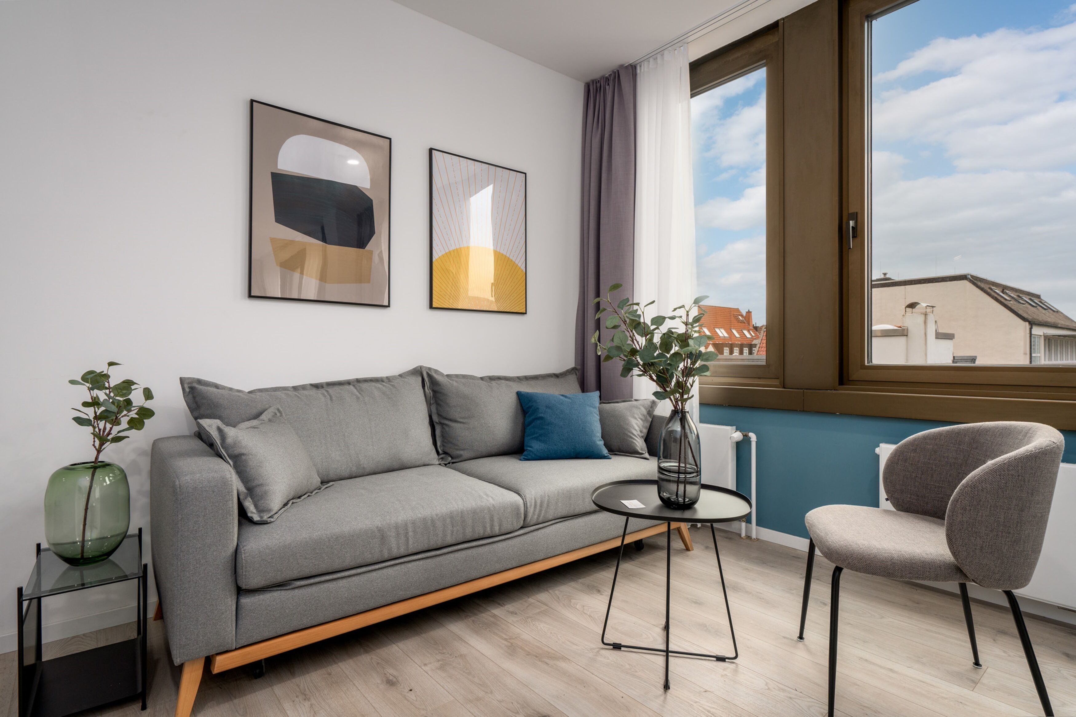 A modern living room with a grey sofa, a round coffee table, a grey armchair, and two framed artworks on the wall.