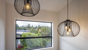 A room with a large window, two hanging pendant lights, and a view of a residential area with trees and houses.