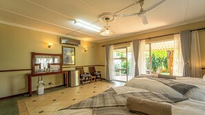 Quarto de hotel com cama, escrivaninha, cadeira, ventoinha no teto e janela com cortinas.
