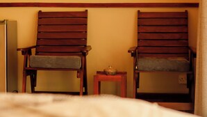 Um quarto com duas cadeiras de madeira, uma mesa pequena com uma tigela e uma cama com cobertura branca.