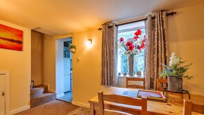 A dining area with a wooden table and chairs, a window with curtains, and a view of a garden. - Stonelea (Tideswell)