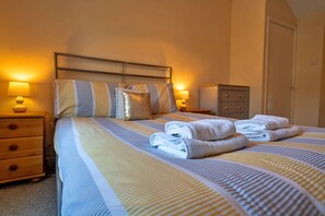 A neatly made bed with striped bedding, two bedside tables with lamps, and a closed door in a hotel room. - Stonelea (Tideswell)