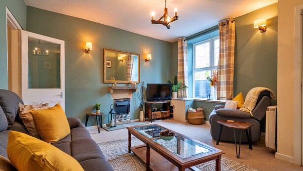 A living room with a sofa, coffee table, TV, fireplace, and a window with curtains. - Stonelea (Tideswell)