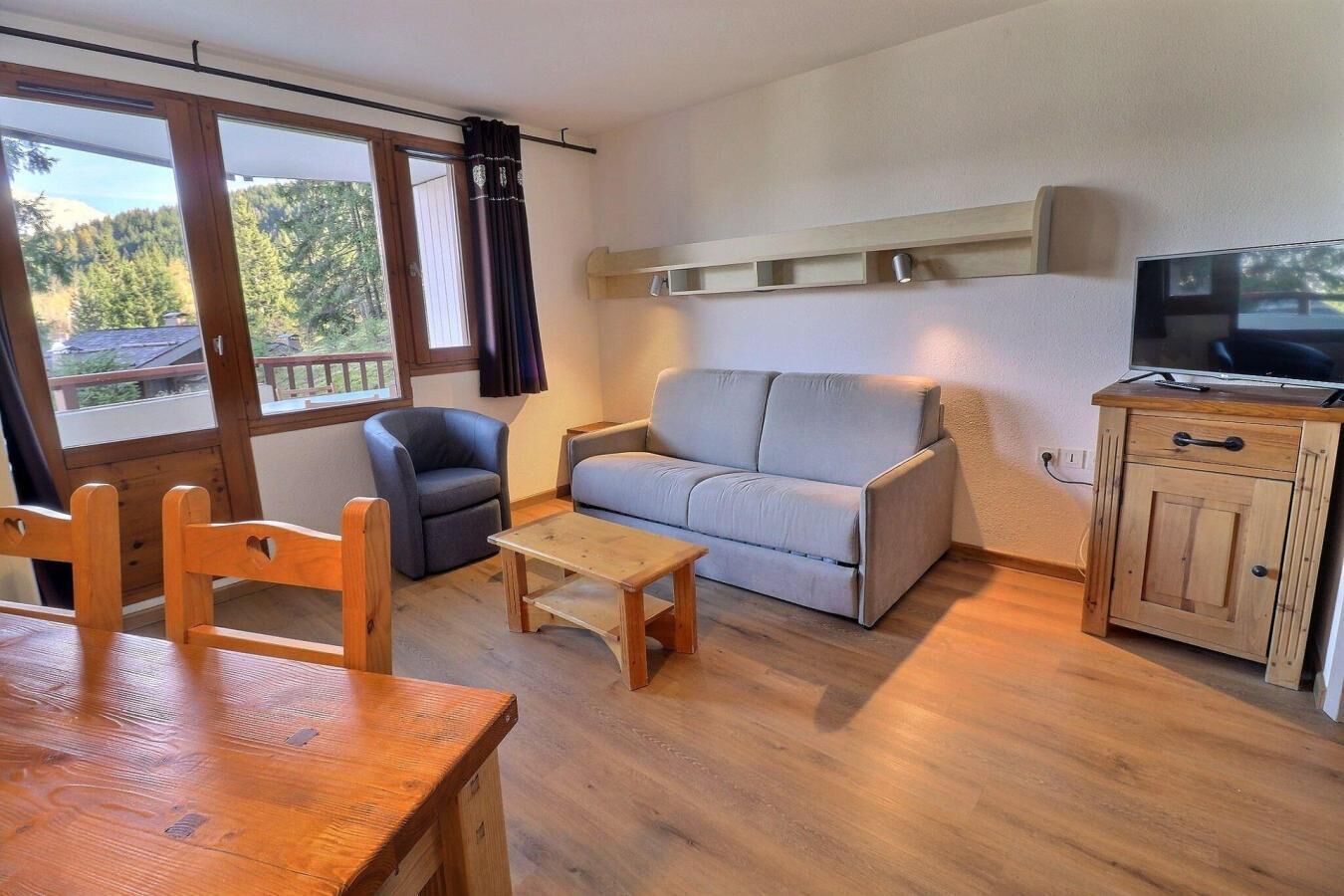 A cozy living room with a sofa, armchairs, a wooden table, and a TV stand.