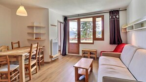 Una habitación con una mesa de madera, sillas, un sofá, una mesita y una ventana con cortinas.