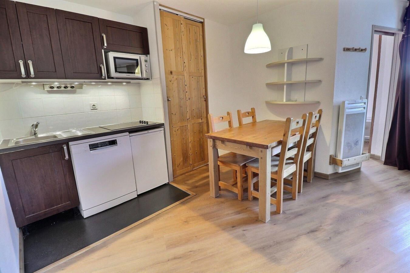 A compact kitchen with a microwave, stove, and dishwasher, a wooden dining table with chairs, and a pendant light.