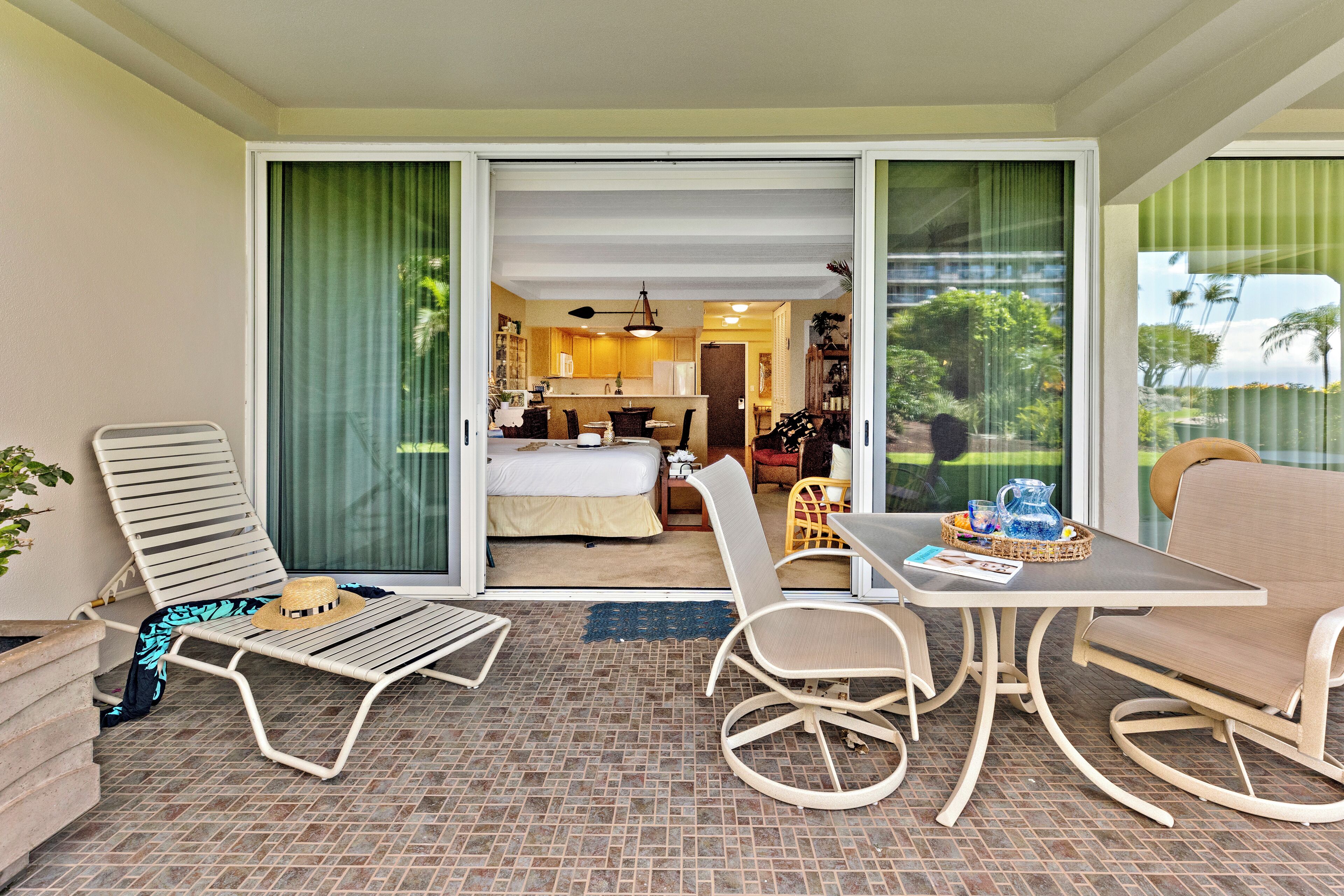 A hotel room with a balcony, a dining area with a table and chairs, and a view of the garden through the glass doors.
