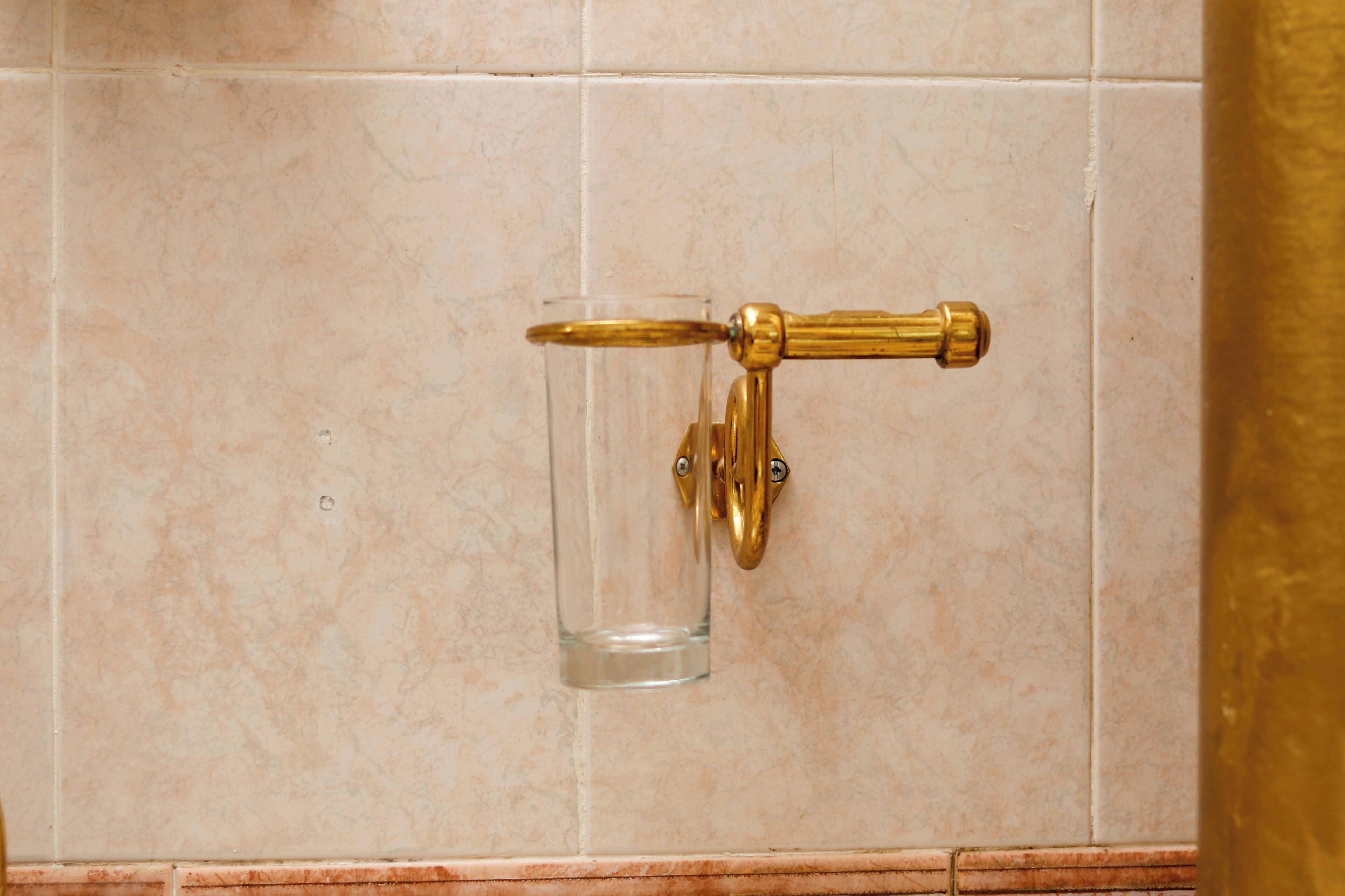 A bathroom with a gold faucet mounted on a tiled wall.