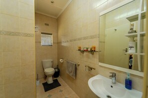 Une salle de bain équipée de toilettes, d’un lavabo, d’un miroir et d’étagères contenant des articles de toilette.