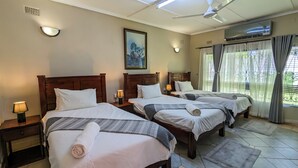 Une chambre d’hôtel avec trois lits, chacun étant équipé d’un oreiller et d’une serviette enroulée. On y trouve également des lampes de chevet, un ventilateur de plafond et un appareil de climatisation.