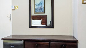 Une pièce avec un bureau en bois, un petit réfrigérateur, un tableau encadré au mur et une porte avec un interrupteur.