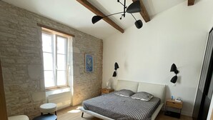 Un dormitorio con una cama grande, una mesita redonda pequeña, una mesita de noche, una pared de piedra y un ventilador de techo.