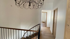 Una escalera con barandilla de madera y baranda de metal negro que conduce a una habitación con candelabro.