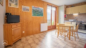 A wooden-paneled room with a dining table and chairs, a television on a cabinet, and a kitchen area with cabinets and appliances. - 150m from ski slopes, 1st floor, balcony, tv, ski locker, 29m², Aussois (Aussois)