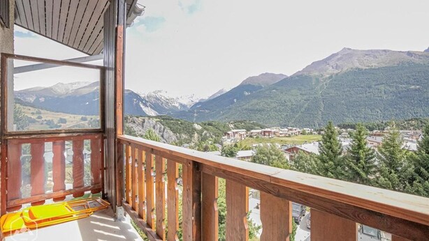 A balcony with a wooden railing overlooking a mountainous landscape with snow-capped peaks and a village below. - 150m from ski slopes, 1st floor, balcony, tv, ski locker, 29m², Aussois (Aussois)