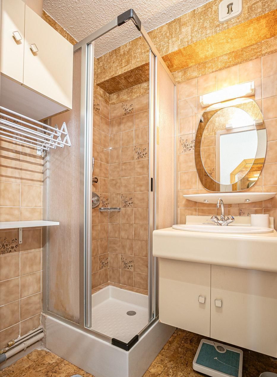 Une salle de bain moderne avec une douche à parois de verre, un lavabo avec un miroir et une balance posée sur le sol.