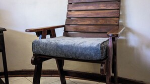 Una silla de madera con cojín azul frente a una pared lisa, sobre suelo de baldosas.