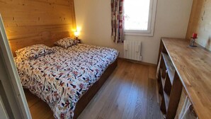 A small, cozy bedroom with a wooden headboard, a bed with floral bedding, a bedside table with a lamp, and a window with curtains.