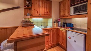 A compact kitchen with wooden cabinets, a sink, a microwave, and a small refrigerator. - 100m from shops, 2nd floor, view ski slopes, balcony, ski locker, 39m², Valmorel (Valmorel)