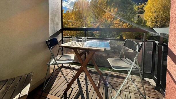 A balcony with a table and chairs, overlooking a scenic view of trees and a distant hill.