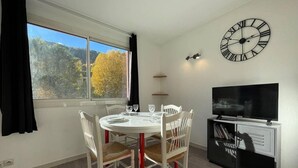 A dining area with a round table, white chairs, and a black TV stand with a clock.