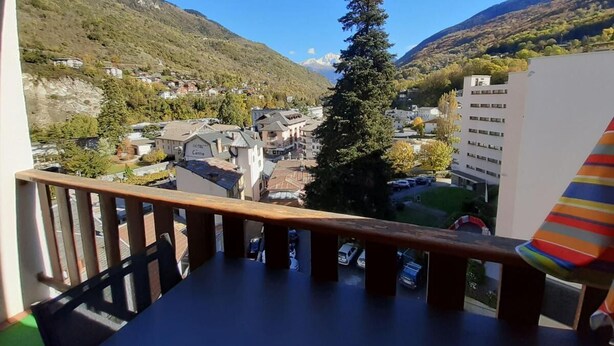 Un balcón con vistas a un pueblo, una montaña y un árbol alto.