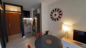 Cocina compacta con electrodomésticos modernos, comedor con mesa y sillas, y un reloj de pared grande.