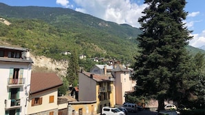 Hotel con vista a la montaña, un gran pino y coches estacionados.