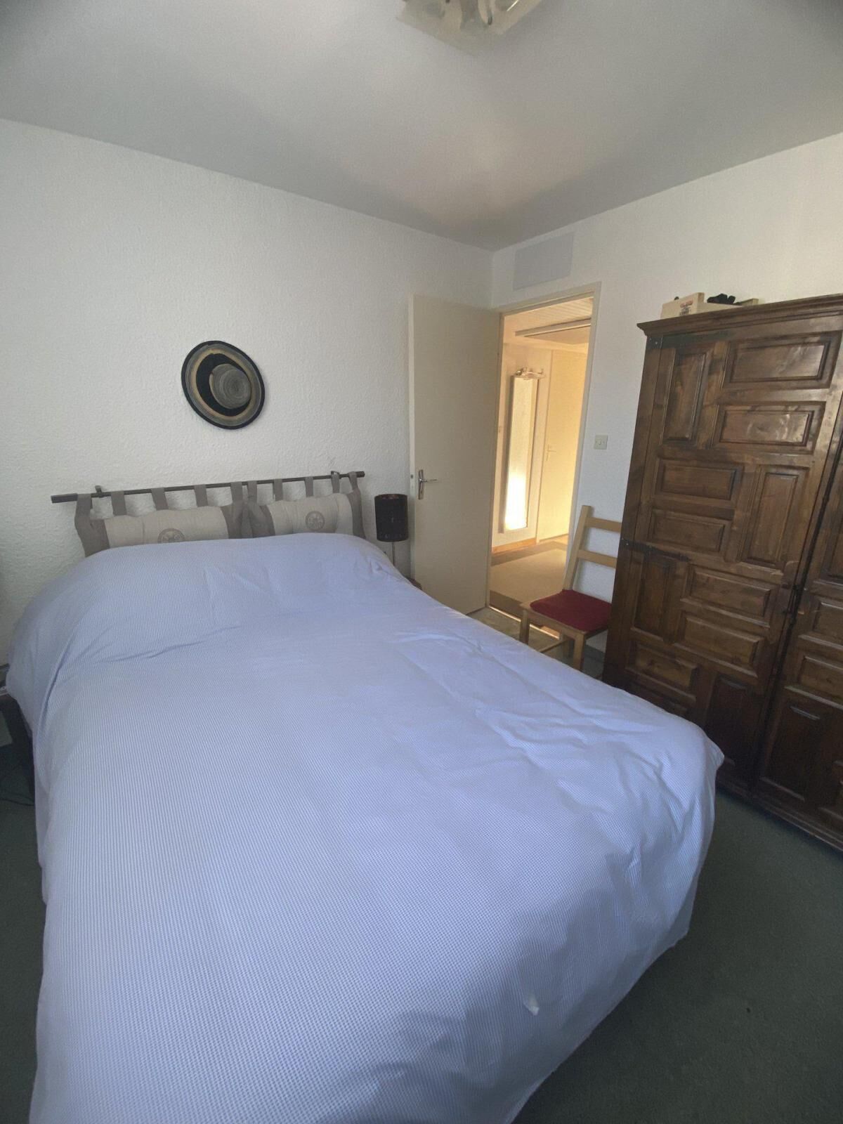 Une chambre avec un grand lit, une armoire en bois, une porte donnant sur une autre pièce et un chapeau accroché au mur.