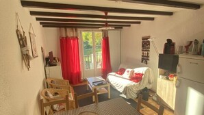 A cozy dining area with a checkered tablecloth, wooden chairs, and a basket of bread. A bed with red curtains and a window is visible in the background. - 1st floor, balcony, tv, 50m², Villard de Lans (Villard-de-Lans)