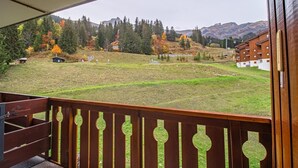 A balcony with a view of a grassy field, trees, and distant mountains.