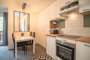 A compact kitchen with a dining table, chairs, a built-in oven, and a microwave.