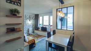 A modern living room with a dining area, a large window, and a plant on a shelf.