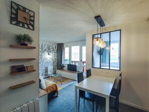 A modern living room with a dining area, a large window, and a plant on a shelf.