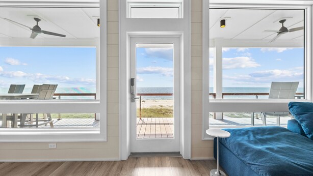 Une pièce avec vue sur la plage, une porte donnant sur l’extérieur, un canapé bleu et des ventilateurs de plafond.