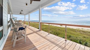 Une terrasse en bois dotée de ventilateurs de plafond, offrant une vue sur une plage et l’océan.