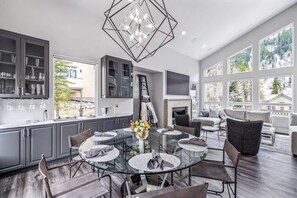 Una cocina moderna con una mesa de comedor de cristal, armarios grises y un ventanal con vistas a un jardín.