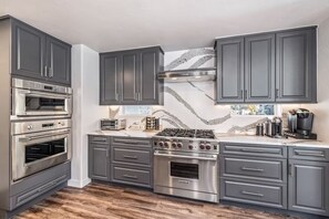 Una cocina moderna con armarios grises oscuros, electrodomésticos de acero inoxidable y un protector contra salpicaduras de mármol.