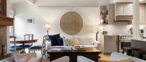 A modern living room with a round coffee table, two armchairs, a sofa, and a dining area with a wooden table and chairs.