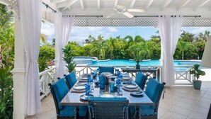 Un espacio cubierto para comer al aire libre con vistas a una piscina y vegetación tropical.