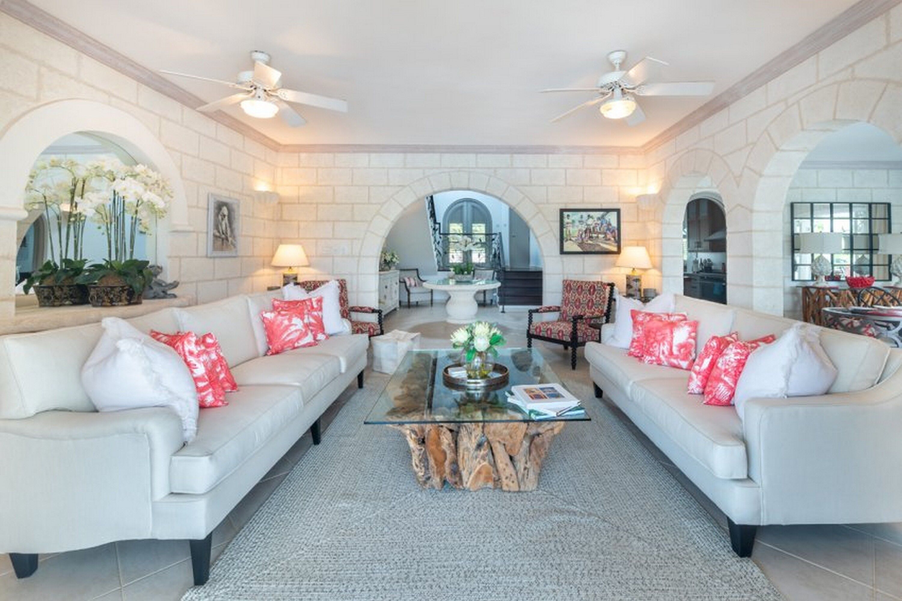 A spacious living room with two white sofas, a glass coffee table, and a fireplace.