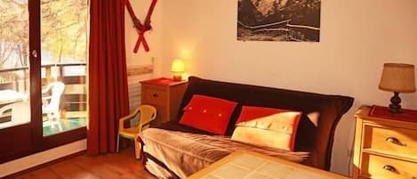 A bedroom with a bed, a nightstand, a chair, a window with curtains, and a wall-mounted picture.