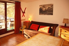 A bedroom with a bed, a nightstand, a chair, a window with curtains, and a wall-mounted picture.